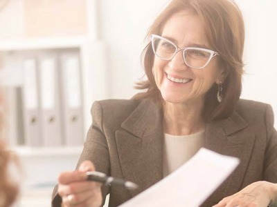 Image of a women smiling pointing to a piece of paper with a pen.